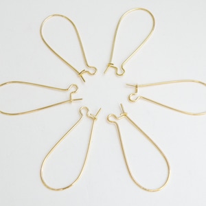 May include: Six gold-toned earring hoops with a teardrop shape. The hoops are arranged in a circle on a white background.
