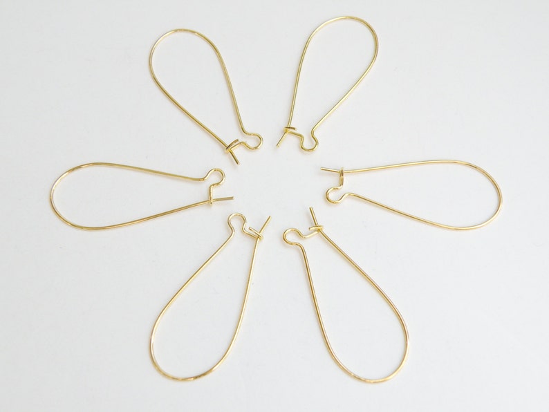 May include: Six gold-toned earring hoops with a teardrop shape. The hoops are arranged in a circle on a white background.