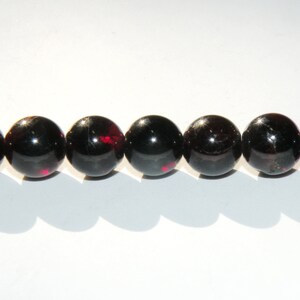 May include: A strand of eight black gemstone beads with red flecks. The beads are round and smooth.