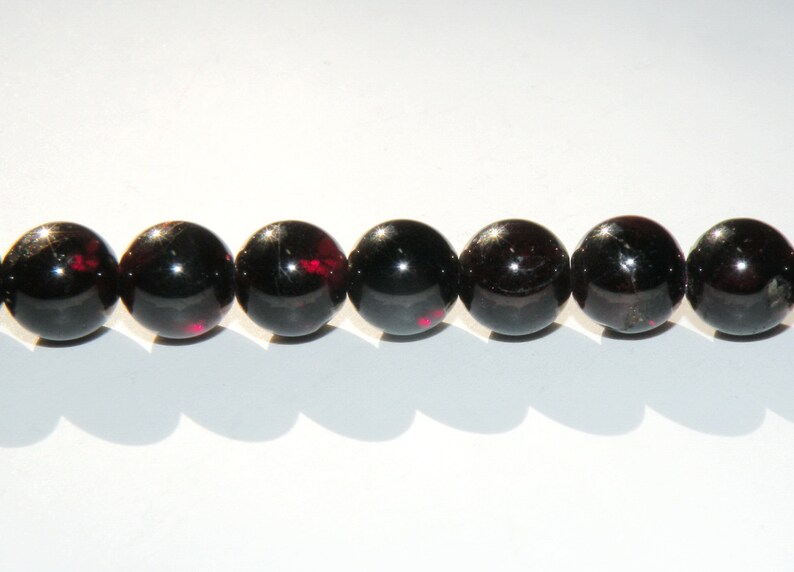 May include: A strand of eight black gemstone beads with red flecks. The beads are round and smooth.