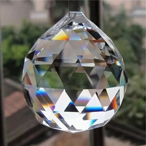 May include: A clear crystal ball with a faceted design. The ball is hanging from a silver string and is reflecting rainbow colors.
