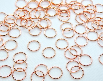 May include: A large quantity of small, gold-colored jump rings. The rings are all the same size and are scattered on a white surface.