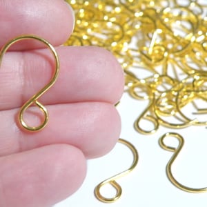 May include: A pile of gold-colored metal hooks. The hooks are small and have a simple design. They are perfect for hanging small items.