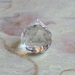 May include: A clear glass crystal prism with a faceted design. The prism is shaped like a teardrop and has a pointed tip.