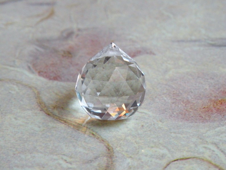 May include: A clear glass crystal prism with a faceted design. The prism is shaped like a teardrop and has a pointed tip.