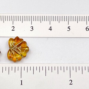 Puede incluir: Dos cuentas de vidrio con forma de hoja, una es &aacute;mbar y la otra es marr&oacute;n con detalles dorados. Las cuentas tienen un di&aacute;metro aproximado de 1 cm.