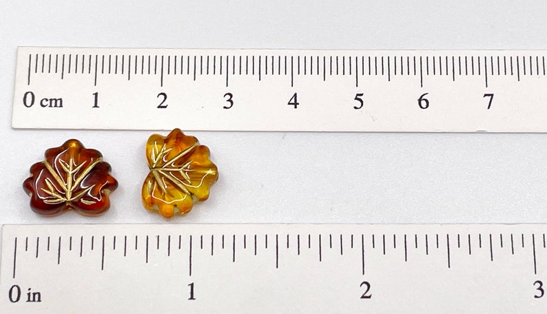 Puede incluir: Dos cuentas de vidrio con forma de hoja, una es &aacute;mbar y la otra es marr&oacute;n con detalles dorados. Las cuentas tienen un di&aacute;metro aproximado de 1 cm.