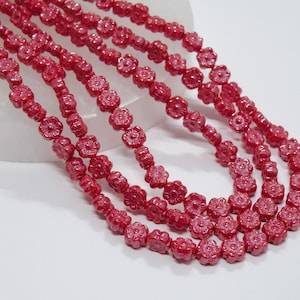 May include: A strand of red glass beads in the shape of flowers. The beads are small and have a slightly iridescent finish.