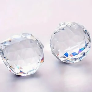 May include: Two clear crystal prisms with faceted surfaces, reflecting rainbow colors. The prisms are round and have a hole at the top for hanging.