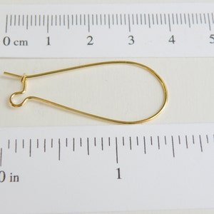 May include: A gold-colored earring finding, measuring approximately 1 inch in length, with a loop at one end and a hook at the other.