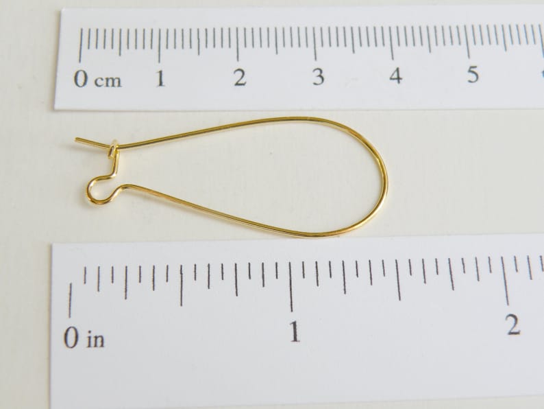 May include: A gold-colored earring finding, measuring approximately 1 inch in length, with a loop at one end and a hook at the other.