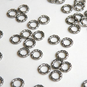 K&ouml;nnte beinhalten: Nahaufnahme eines Stapels silberner Sprungringe. Die Ringe sind klein und haben ein gedrehtes Design.