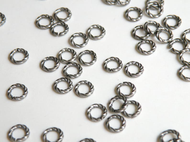 K&ouml;nnte beinhalten: Nahaufnahme eines Stapels silberner Sprungringe. Die Ringe sind klein und haben ein gedrehtes Design.