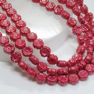 May include: A strand of red glass beads with a flower design. The beads are strung together to form a necklace.