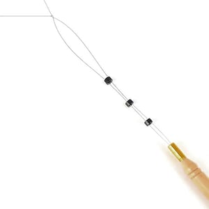 May include: A hair extension tool with a wooden handle and a gold-colored ferrule. The tool has a thin wire loop with small black beads attached. The background is plain white.