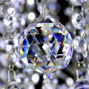 May include: A large, clear crystal ball with a faceted design. The ball is hanging from a silver chain and is surrounded by other smaller crystals.
