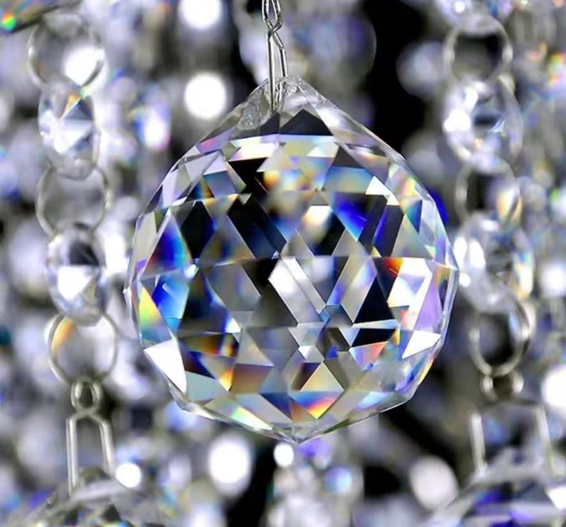 May include: A large, clear crystal ball with a faceted design. The ball is hanging from a silver chain and is surrounded by other smaller crystals.
