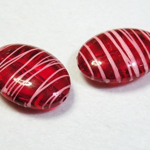May include: Two oval-shaped glass beads with a red base and white stripes.