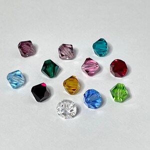 May include: Assortment of 12 faceted glass beads in various colors, including clear, red, green, blue, purple, and gold. The beads are all the same size and shape, and they are arranged in a circle on a white background.