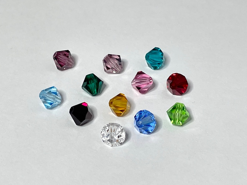 May include: Assortment of 12 faceted glass beads in various colors, including clear, red, green, blue, purple, and gold. The beads are all the same size and shape, and they are arranged in a circle on a white background.