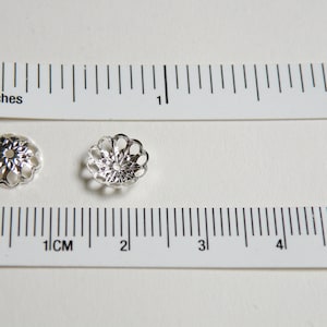 May include: Two silver-toned metal bead caps with a decorative, openwork design. The caps are approximately 1 cm in diameter.