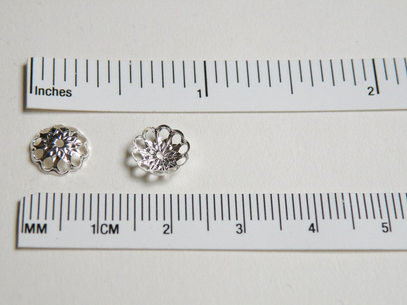 May include: Two silver-toned metal bead caps with a decorative, openwork design. The caps are approximately 1 cm in diameter.