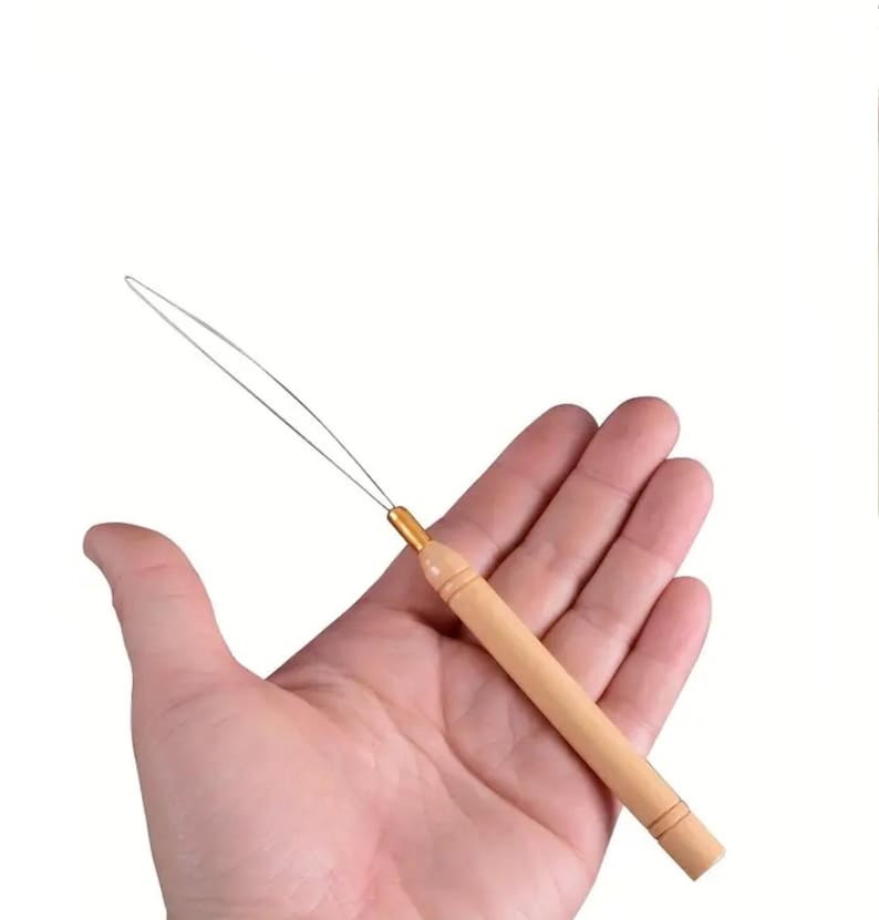 May include: A hair extension tool with a light wooden handle and a thin metal loop. The handle has a gold-colored metal accent at the top. The tool is designed for applying hair extensions.