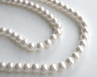 May include: A strand of lustrous, off-white pearls. The pearls are round and evenly sized, reflecting light with a soft sheen. The necklace is arranged in a curved pattern, suggesting it is ready to be worn. A classic jewelry piece.