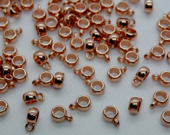 May include: A collection of rose gold-colored jewelry findings, including small, rounded connector bails with a loop for attaching to other jewelry components. The findings are scattered across a light-colored surface, reflecting light.