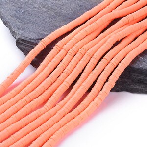 Könnte beinhalten: Eine Schnur aus korallenorangen Polymer-Tonperlen. Die Perlen sind flach und rund und auf einem durchsichtigen Faden aufgefädelt. Die Perlen sind versetzt angeordnet.