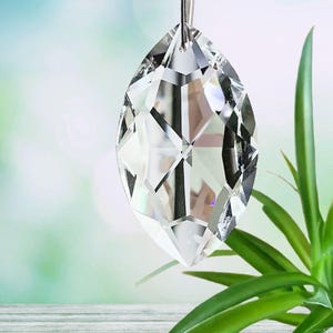 May include: A clear crystal prism with a faceted design, hanging from a silver chain. The prism is shaped like a teardrop and is reflecting light.