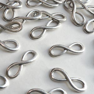 May include: A collection of silver infinity symbol charms. The charms are small and delicate, perfect for adding a touch of elegance to jewelry or crafts.