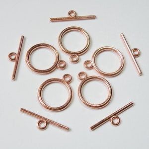 May include: A set of eight rose gold toggle clasps for jewelry making. The clasps are made of metal and have a round shape with a bar that slides through the loop.
