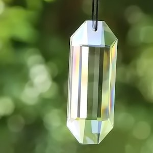 May include: A clear crystal prism pendant with a faceted design, hanging from a black cord. The prism reflects light, creating rainbow colors.