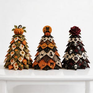 May include: Three decorative fabric trees featuring Halloween themes. The left tree has orange pumpkins and green leaves. The center tree displays black cats and pumpkins. The right tree features skulls and roses, topped with a dark red fabric rose.