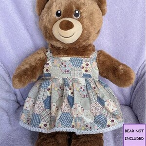 May include: A brown plush teddy bear wearing a sleeveless dress with a multi-coloured hexagonal patchwork pattern featuring floral and geometric designs, finished with a white lace trim at the hem. The text BEAR NOT INCLUDED is visible.