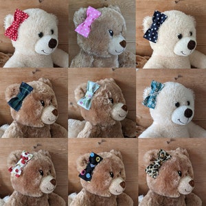 May include: Nine teddy bears with different patterned bows on their heads. The bows are in various colours and patterns, including plaid, floral, polka dots, and animal print.