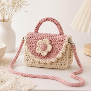 Può includere: Borsa a mano all'uncinetto fatta a mano in rosa e crema. La borsa presenta un'applicazione floreale e un bordo smerlato. Ha un manico superiore e una tracolla staccabile. La borsa è larga circa 20 cm e alta 15 cm.