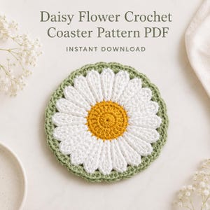 May include: A handmade crochet daisy coaster with a white flower design, yellow center, and green border. The text "Daisy Flower Crochet Coaster Pattern PDF" and "Instant Download" are displayed at the top of the image.