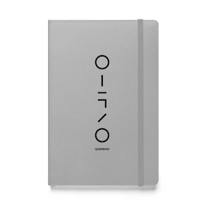 May include: A gray notebook with a black geometric design and the word "QUEERKIND" printed at the bottom. The notebook has an elastic band closure and a minimalist design.