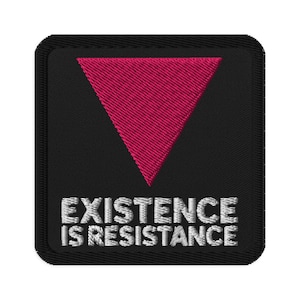 Puede incluir: Parche bordado con fondo negro, un triángulo rosa y el texto blanco "EXISTENCE IS RESISTANCE". El parche tiene forma cuadrada con esquinas redondeadas y un borde negro.