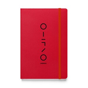 May include: A red notebook with a matching elastic band closure. The cover features a vertical black graphic and the word "QUEERIOND" in a sans-serif font. The notebook is rectangular and has a textured surface.