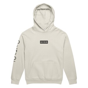 Pode incluir: Moletom creme com bolso frontal e capuz. A palavra "QUEERKIND" é impressa em um retângulo preto no peito. A manga esquerda tem as palavras "DIVERSITY" e "PRIDE" impressas verticalmente em preto.