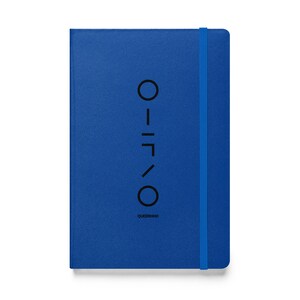 May include: A cobalt blue notebook with an elastic band closure. The cover has a vertical design and the text "QUEERKING" at the bottom. The design includes a series of black geometric shapes.