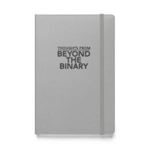 May include: A light grey notebook featuring the text "THOUGHTS FROM BEYOND THE BINARY" in black. It has a matching grey elastic band closure.