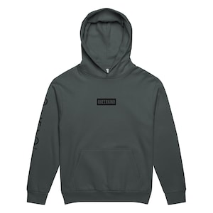 May include: A dark gray hoodie with a front pocket and a hood. The word "QUEERKIND" is printed in a black rectangle on the chest. The left sleeve has the word "QUEER" printed vertically in black.