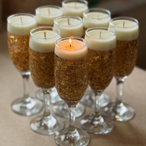 Puede incluir: Un conjunto de velas en copas de champán. La mitad inferior de cada copa está cubierta con pan de oro. Las velas son blancas y tienen una mecha encendida. Las copas están dispuestas en círculo.