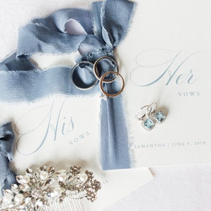 Op de afbeelding: Twee witte gelofteboekjes met de tekst His Vows en Her Vows, blauw zijden lint, drie zilveren ringen, een paar lichtblauwe vierkante oorbellen en een zilveren haarkam met heldere kristallen en witte parels, gedateerd 9 juni 2018 voor Samantha.