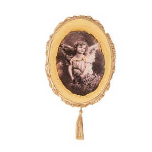 May include: Oval-shaped wooden frame with a sepia-toned image of a child with angel wings holding flowers. The frame has a natural wood grain edge and a gold tassel hanging from the bottom. The image has text at the top.