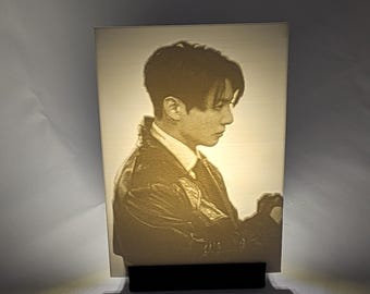 May include: A rectangular lithophane light panel featuring a monochromatic portrait of a person in profile, wearing a collared shirt and a jacket. The image is illuminated from behind, creating a warm glow, and is supported by a black stand.